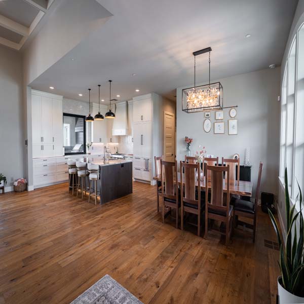Riddle_Construction_Water_Hazard_Dining Open-plan kitchen and dining area with white cabinets, a dark island and six bar stools, and a wooden dining table by a large window.
